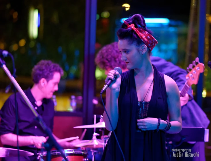 a young woman holding a microphone and singing in front of band