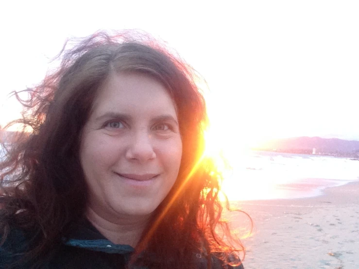 a woman stands on the beach while the sun shines on her hair