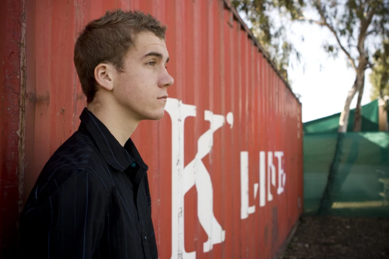 a young man is leaning against a red wall