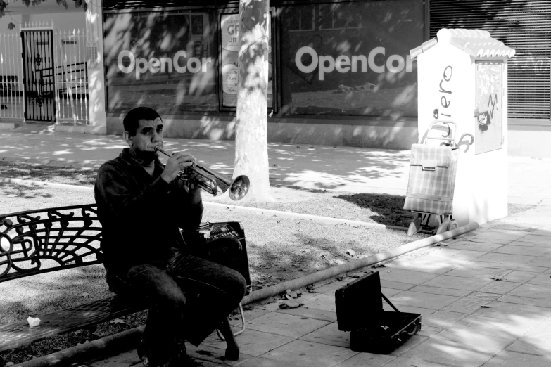 man playing trumpet on the street bench in front of a sign