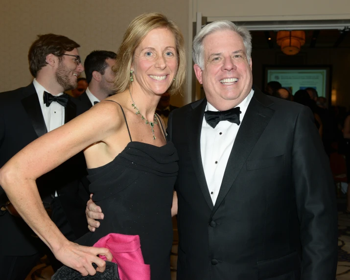 two people smiling with tuxedos in the background