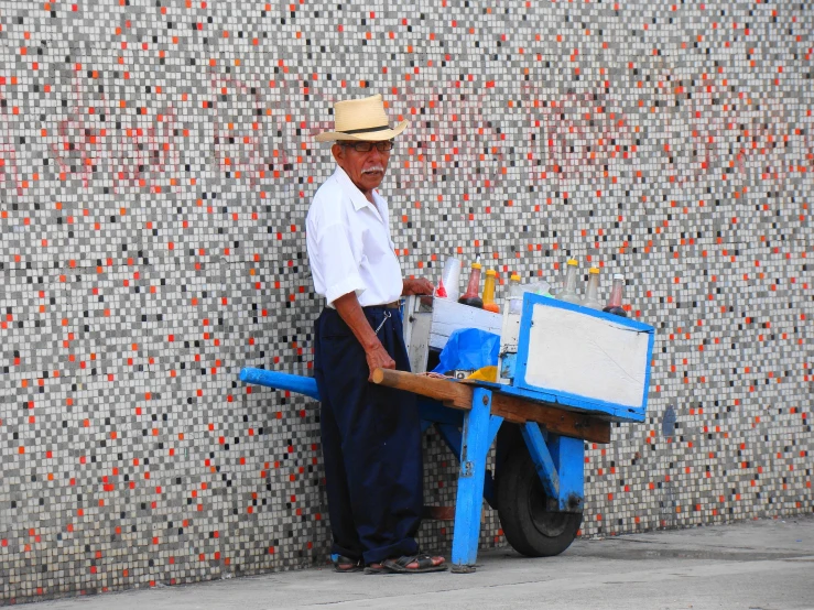 an old man stands by a blue cart that sells jugs and other things