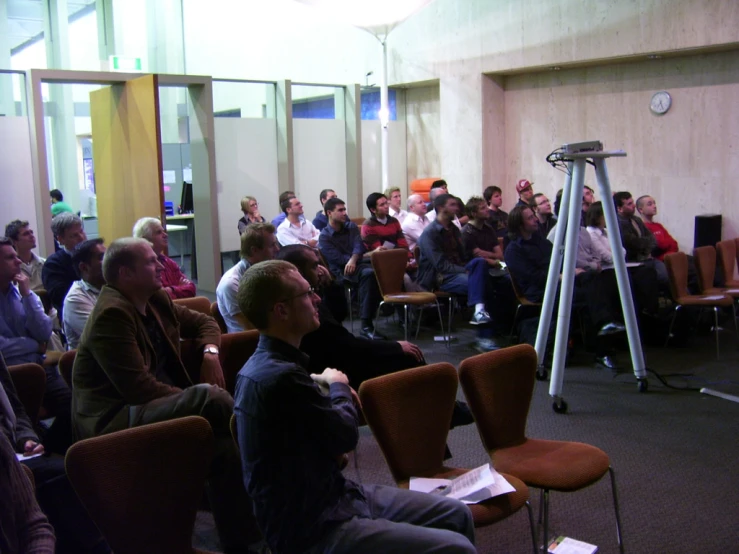 a crowd of people are sitting in chairs listening to someone standing at the front of the room