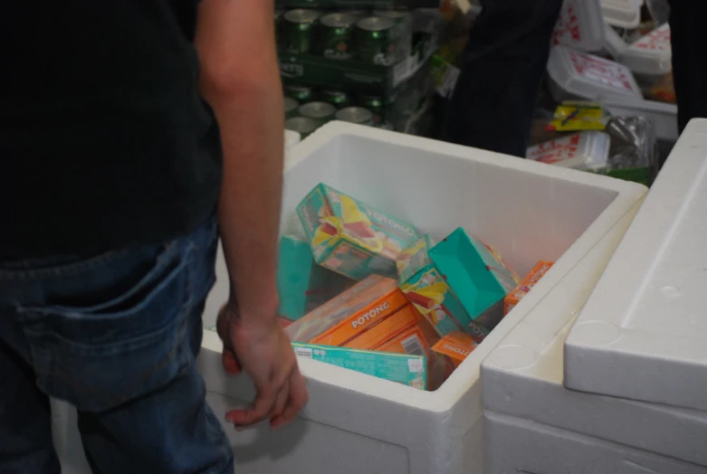 a man's hand coming out of a large white bin filled with fruit and vegetables