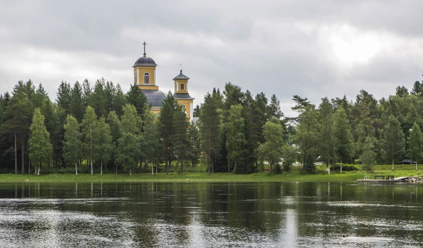 a church is on the side of a lake surrounded by trees