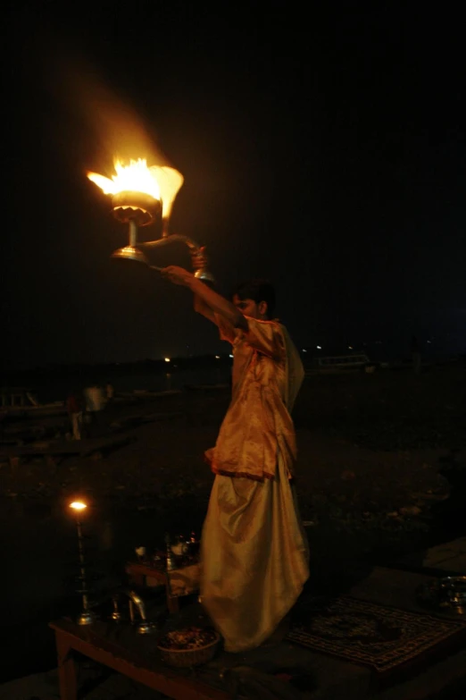 woman holding lit lamp in air near river at night