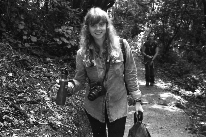 a woman walking down a dirt road with a camera in hand