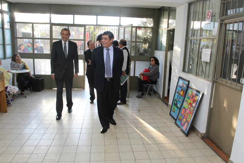 two men walking down a hall that has some windows