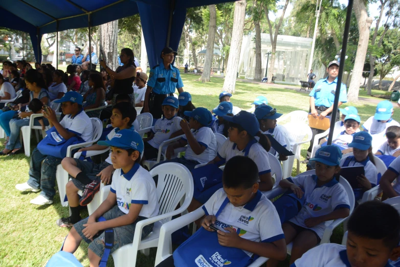 many children sit in white chairs under a blue canopy