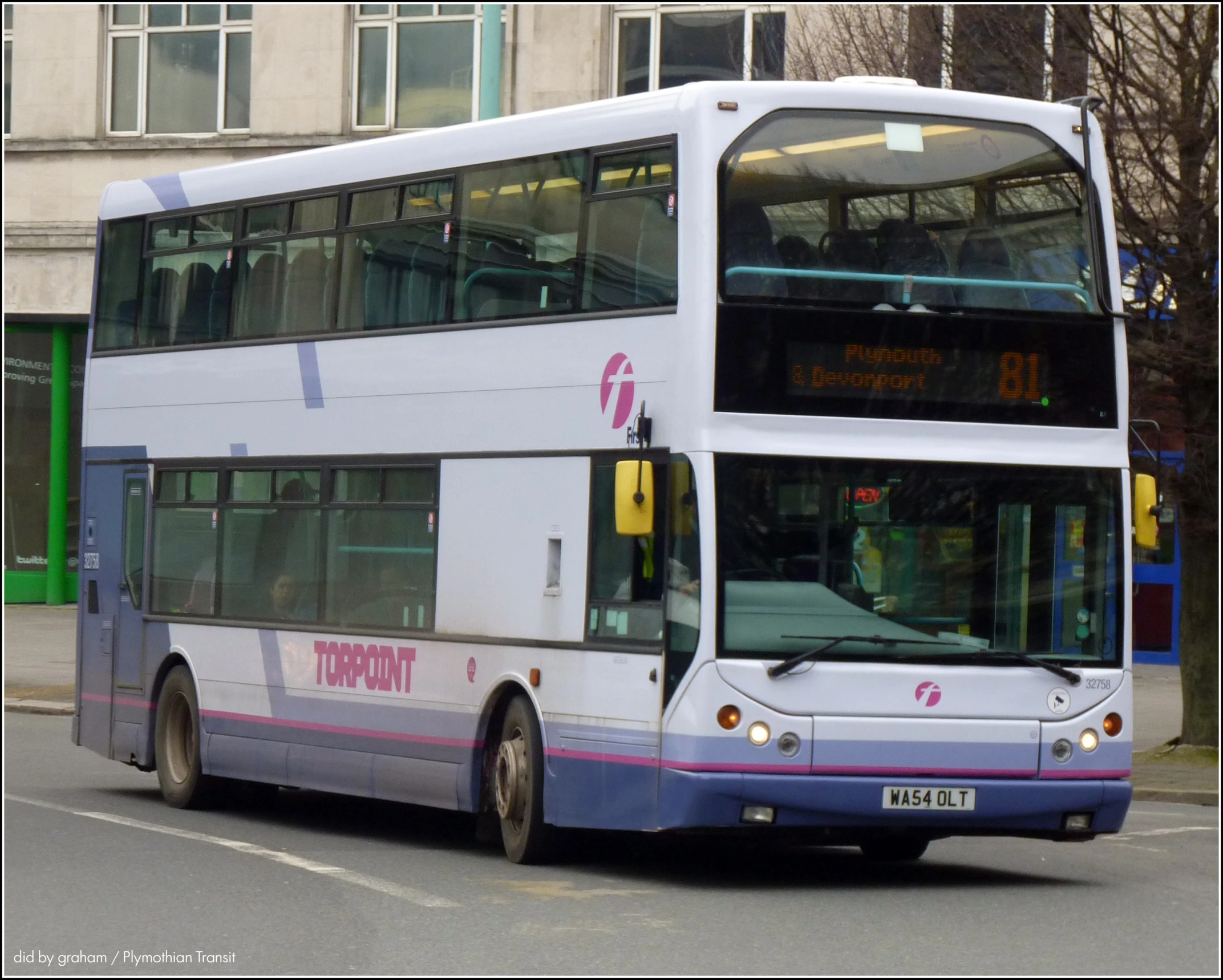 double decker bus coming down the road near a building