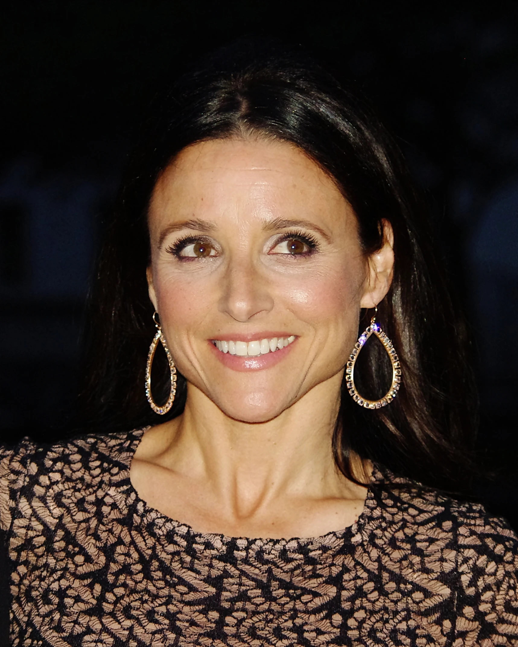 a woman smiling for the camera wearing a patterned dress and large gold hoop earrings