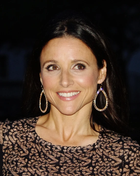 a woman smiling for the camera wearing a patterned dress and large gold hoop earrings