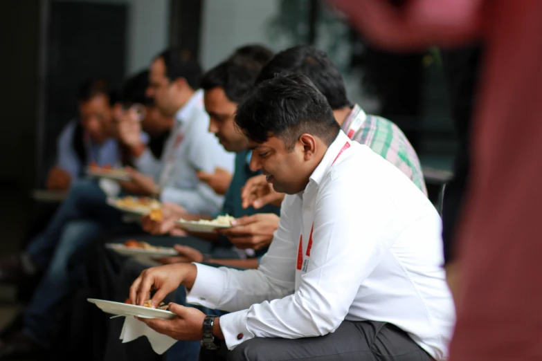 several people are sitting at tables looking at paperwork and eating plates of food