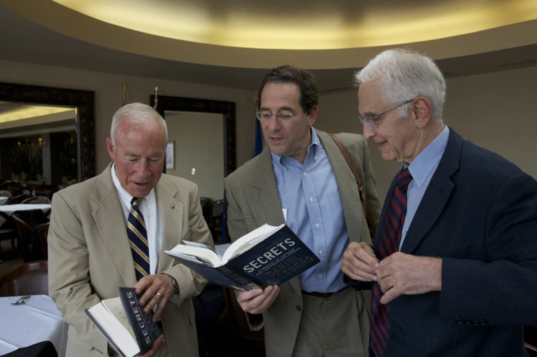 three men in suit standing together and one holding a book