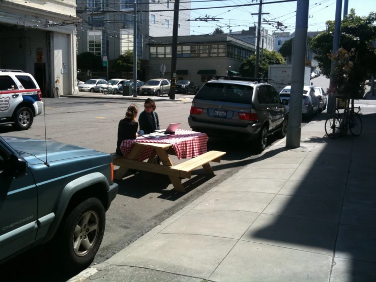 two people sit at a picnic table by the road