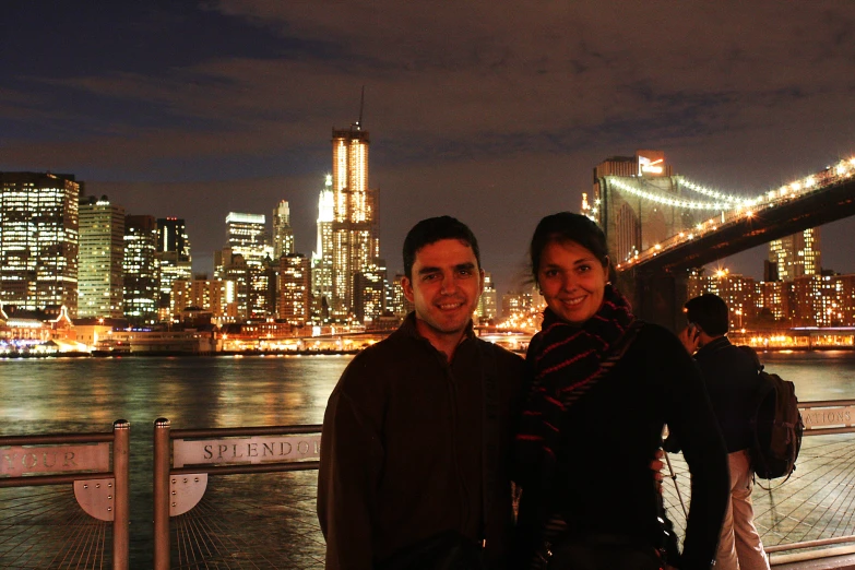 two people standing on a bridge with a city behind them