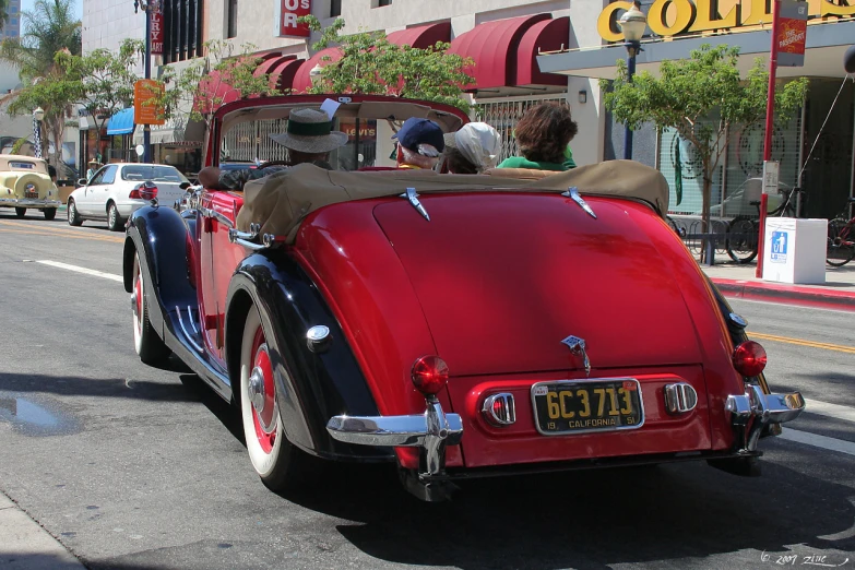 two people in an old fashioned car driving through a town