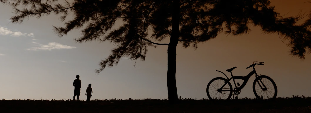 silhouettes of a bike, a person and two small children standing by a tree