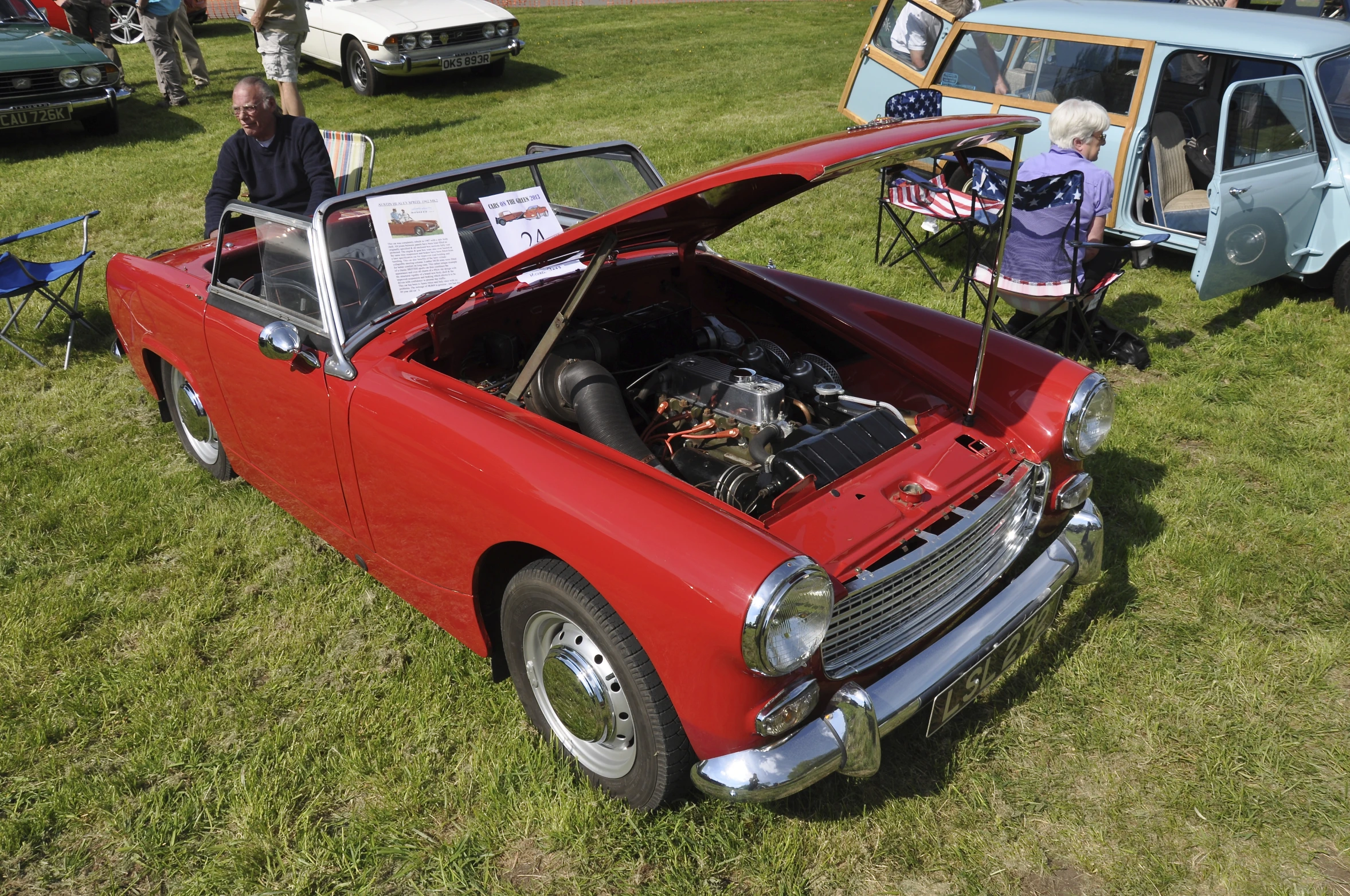 a red car parked in a field with other old cars