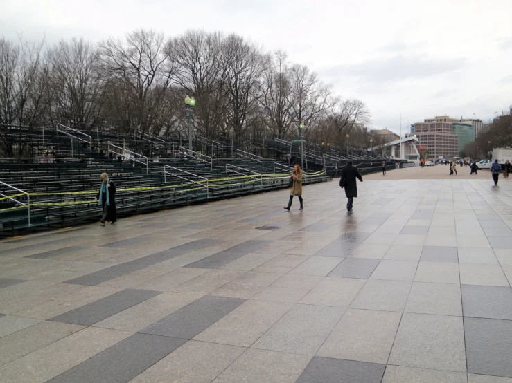 several people walking on the sidewalk near a stadium