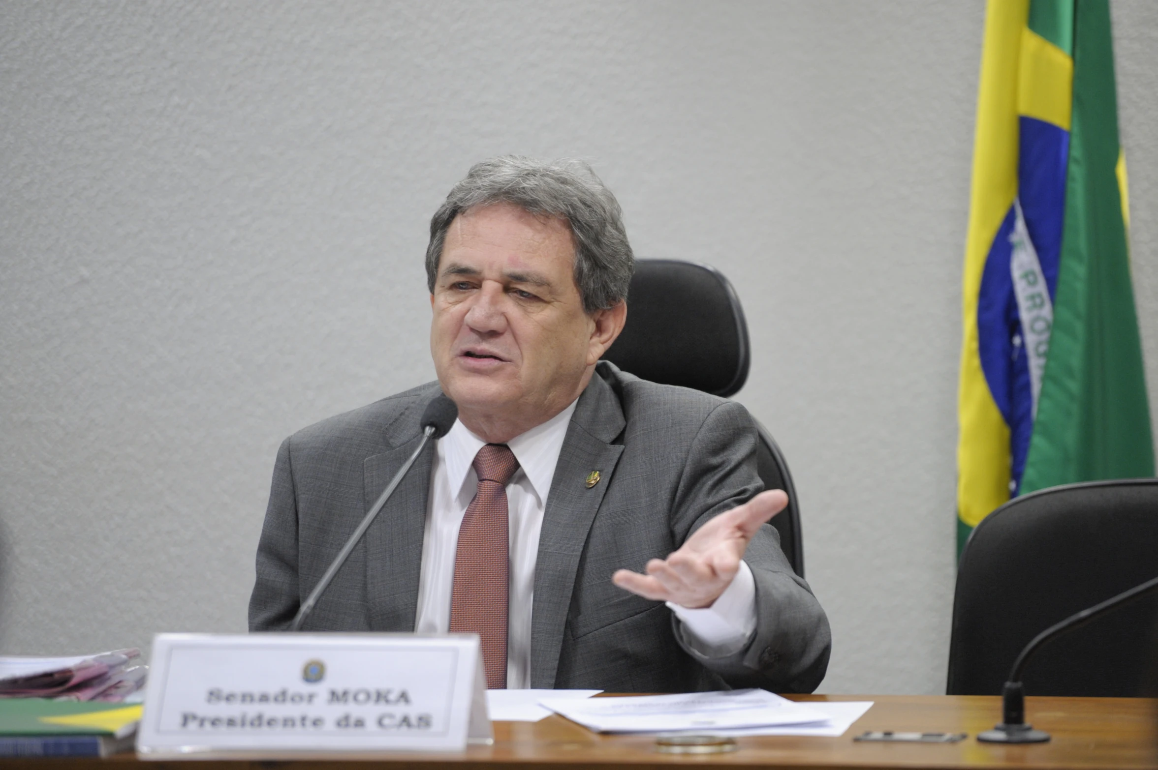 a man in a suit sitting at a table in front of a microphone and papers