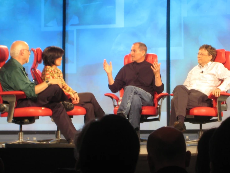 two men and a woman sitting in red chairs on a stage