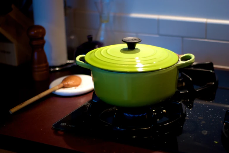 a green pot with spoon on top of a stove