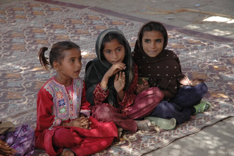 three children in colorful clothing sitting on carpet
