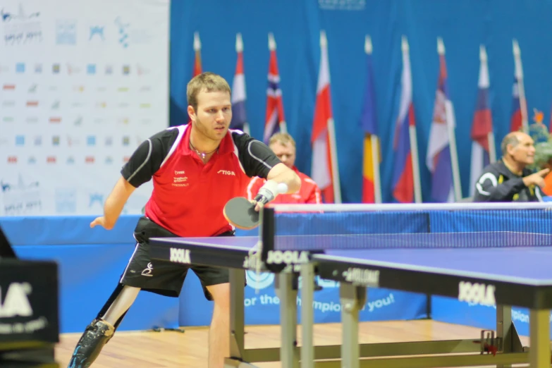 a man in red shirt and black shorts playing ping pong