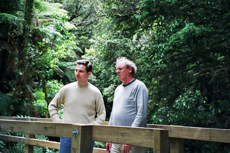 two men standing near a wooden bridge in the woods