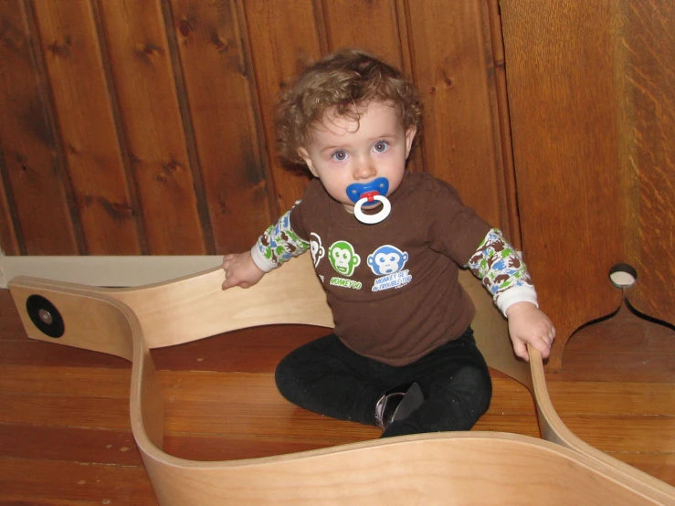 a young toddler sits on a wooden chair while holding a pacifier