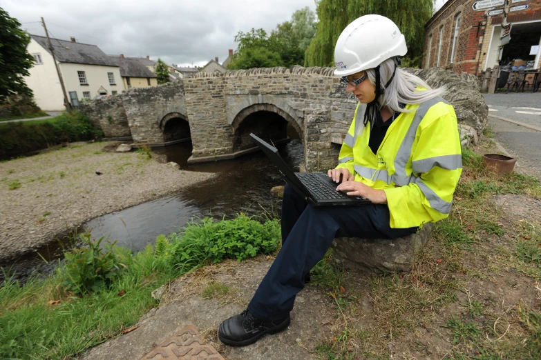 woman in yellow safety gear using a laptop