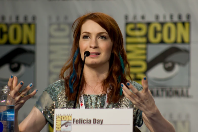 a woman with red hair speaking to the crowd at a convention