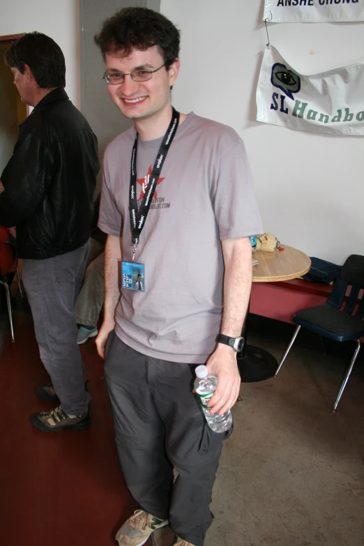 a man in glasses and a gray shirt smiles as he stands next to a table with other men