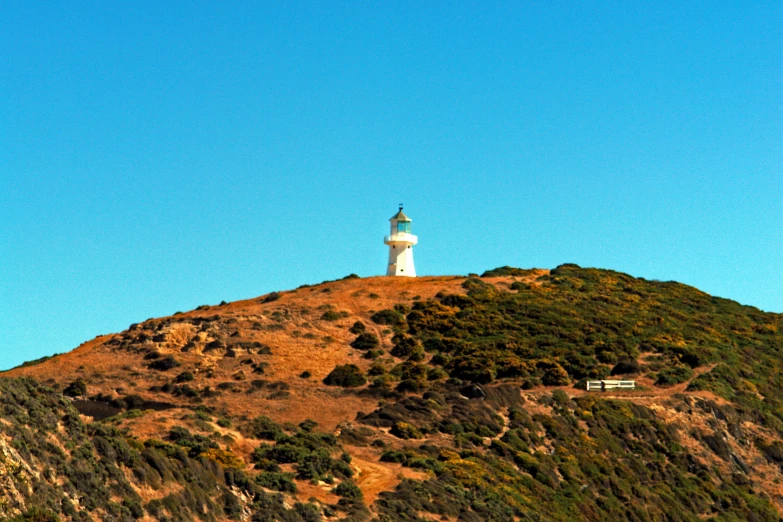 a tall white light house on top of a grassy hill