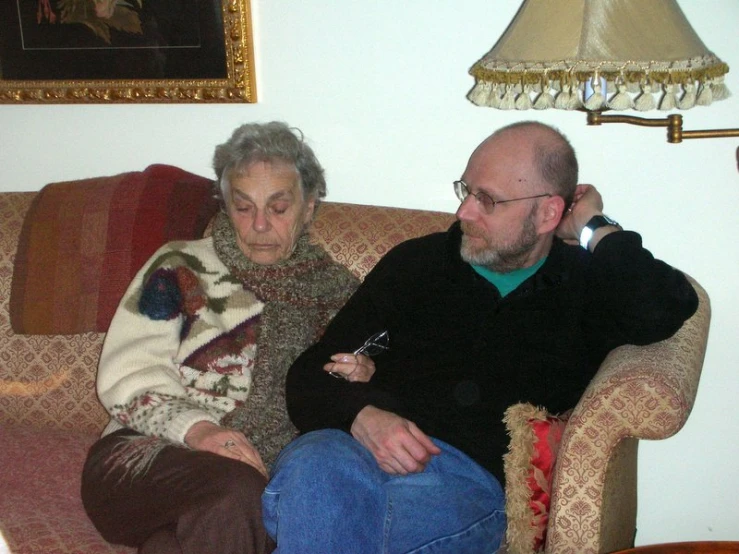 an old couple sit on a couch and stare at the camera