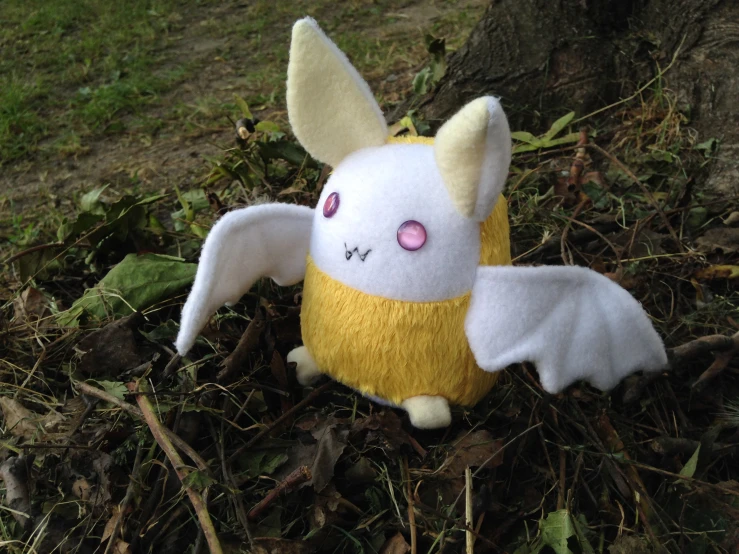 a stuffed animal with big eyes and wings on a forest ground