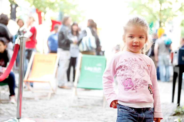 little girl wearing jeans standing in front of a crowd