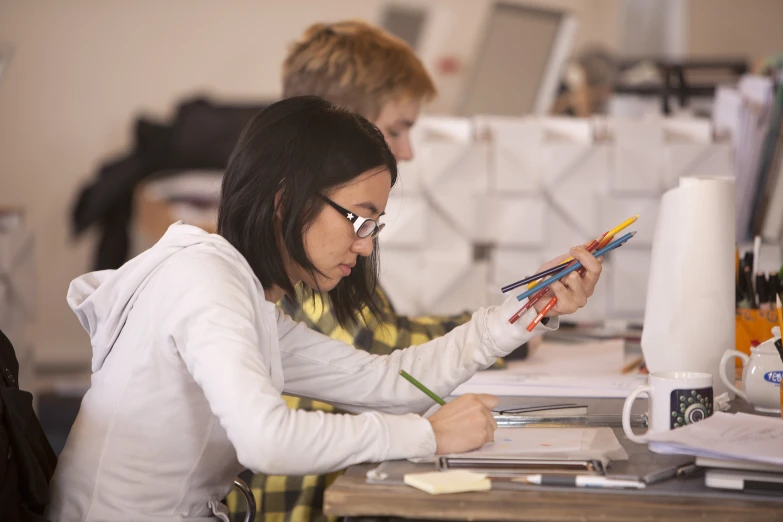 a woman sits at a desk while drawing with colored pencils