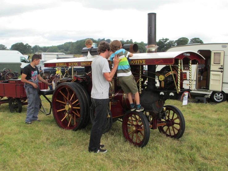 people standing near a small, old fashioned locomotive in a field