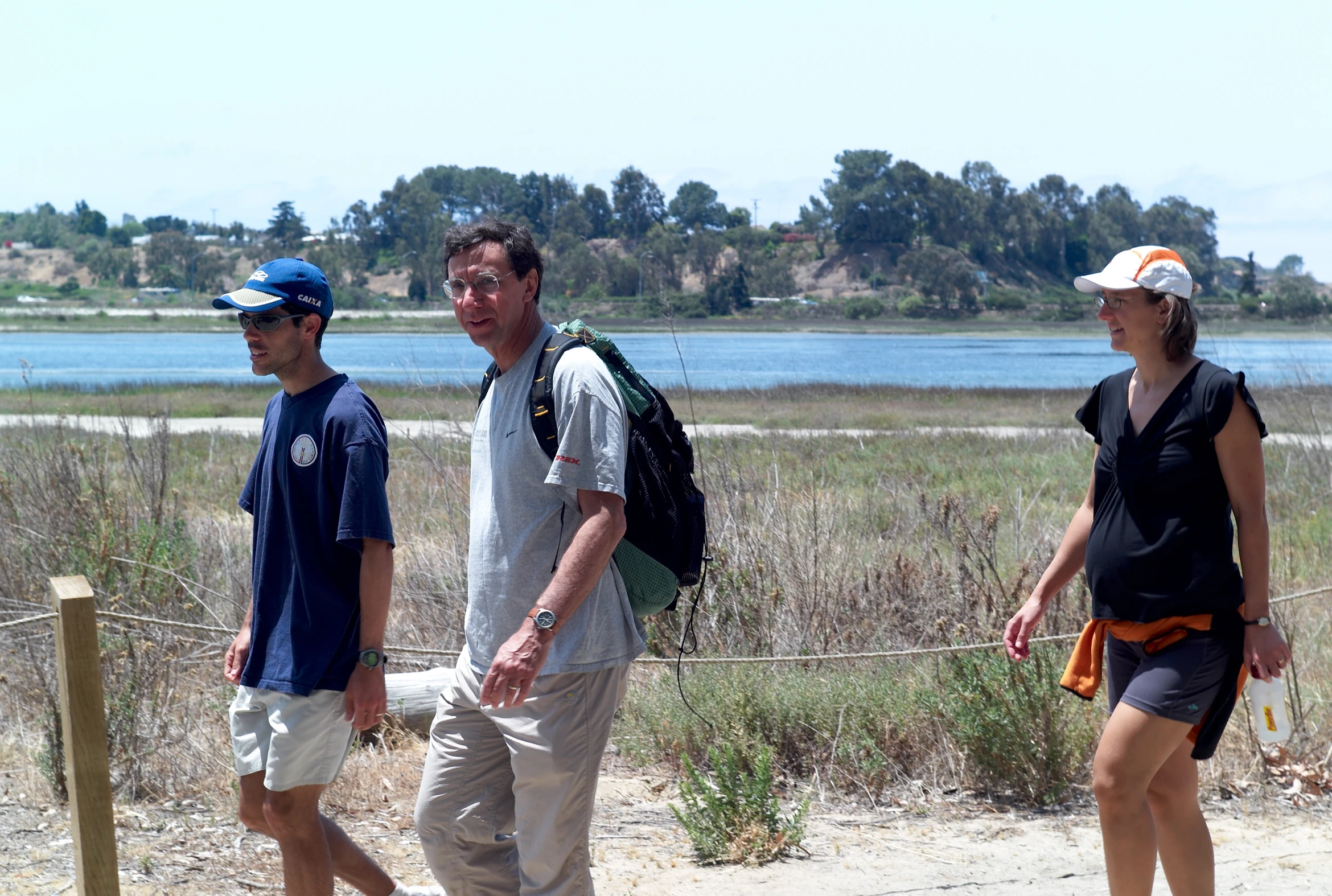 three people walking on the sand with a river in the background