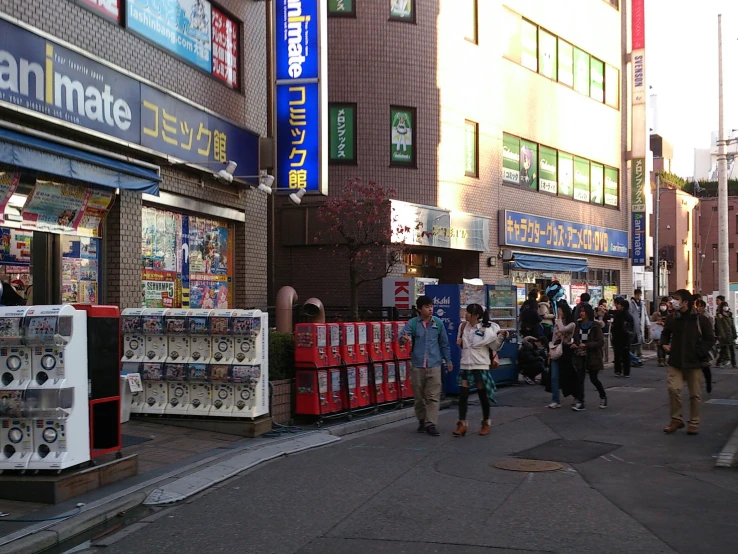 an asian street with people walking down the road and several vending machines