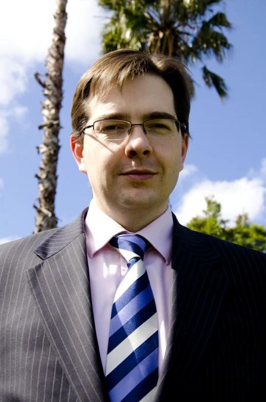 a man in a suite and tie in front of trees