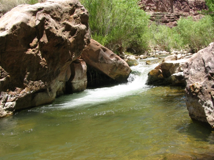 a stream running between large rocks and a green body of water