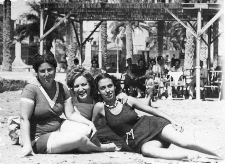 three young women, two posing for a po, are sitting on the beach