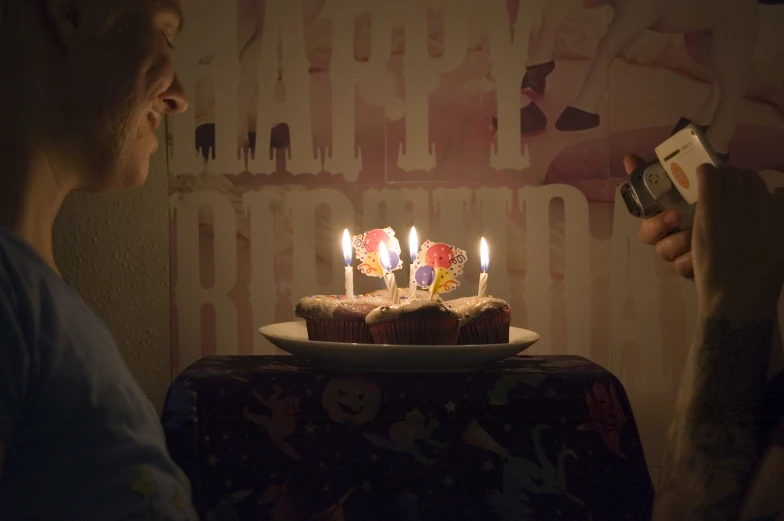 a woman taking a picture with her cell phone with a birthday cake on the table