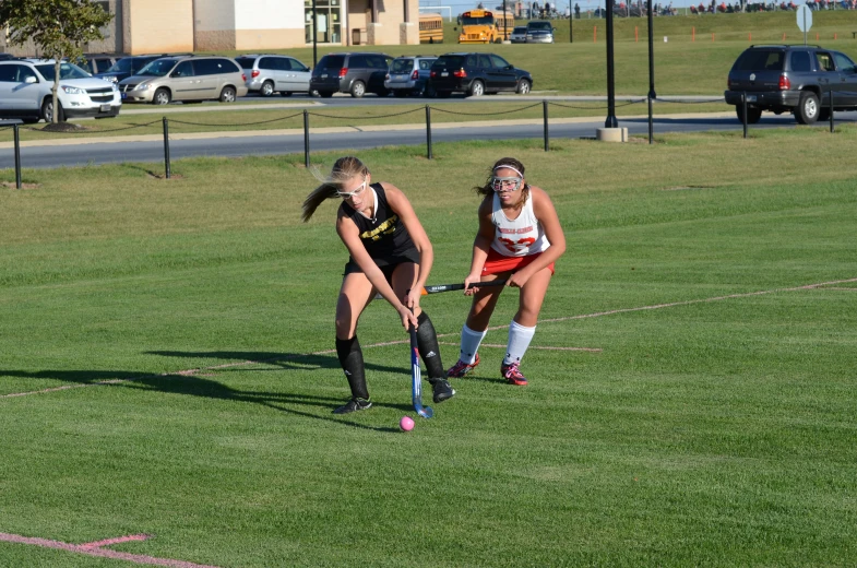 two female field hockey players, one playing in the grass