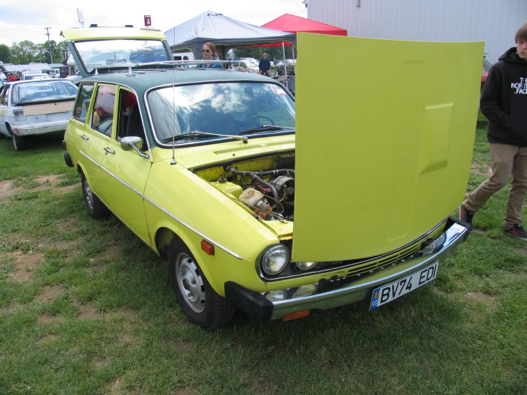 a man stands beside a very old yellow car