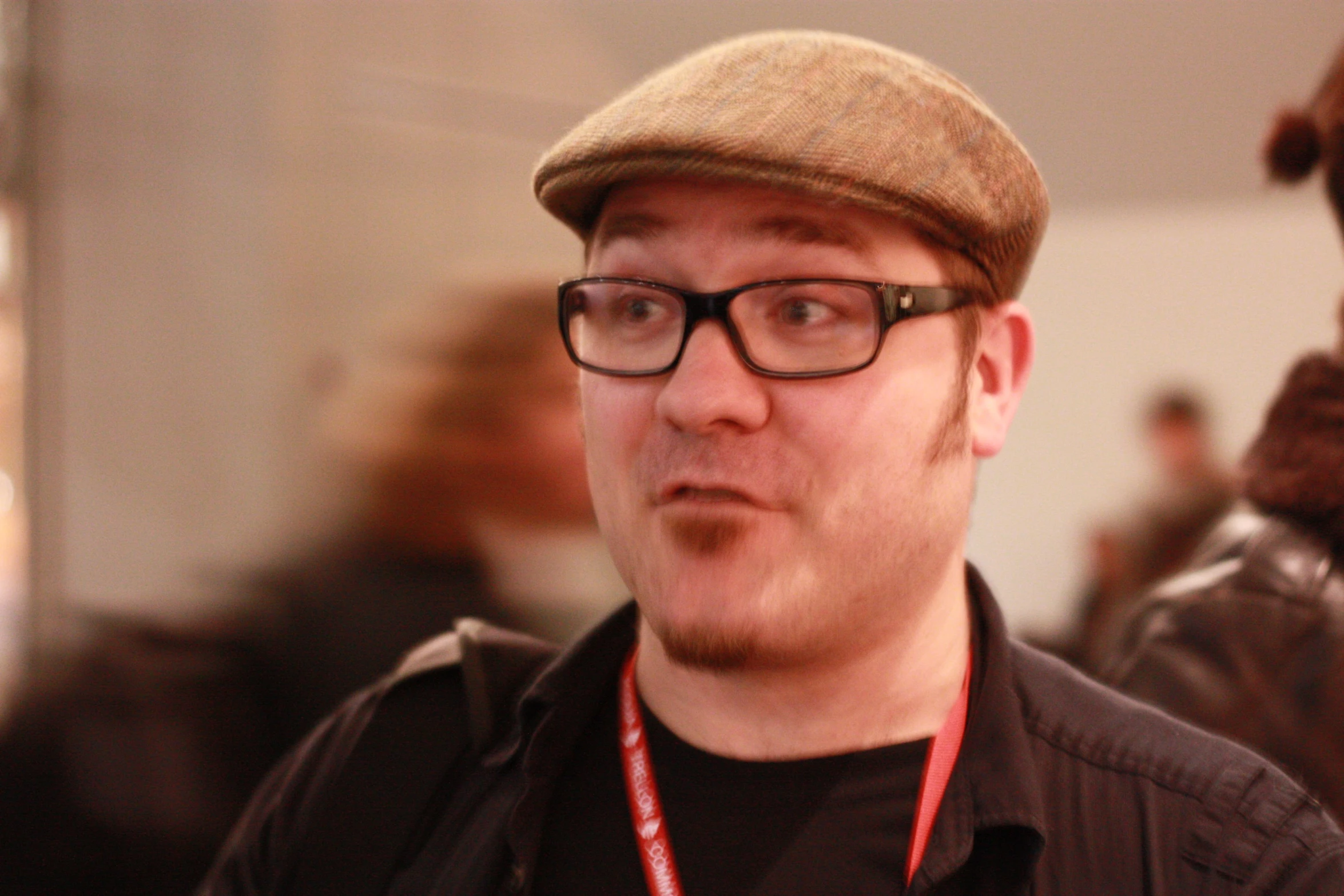 man with glasses and a hat wearing a red lanyard