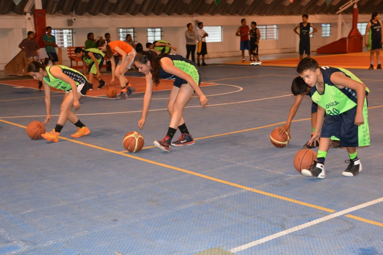 three children in green and black uniforms hold basketballs while wearing matching orange and blue shirts